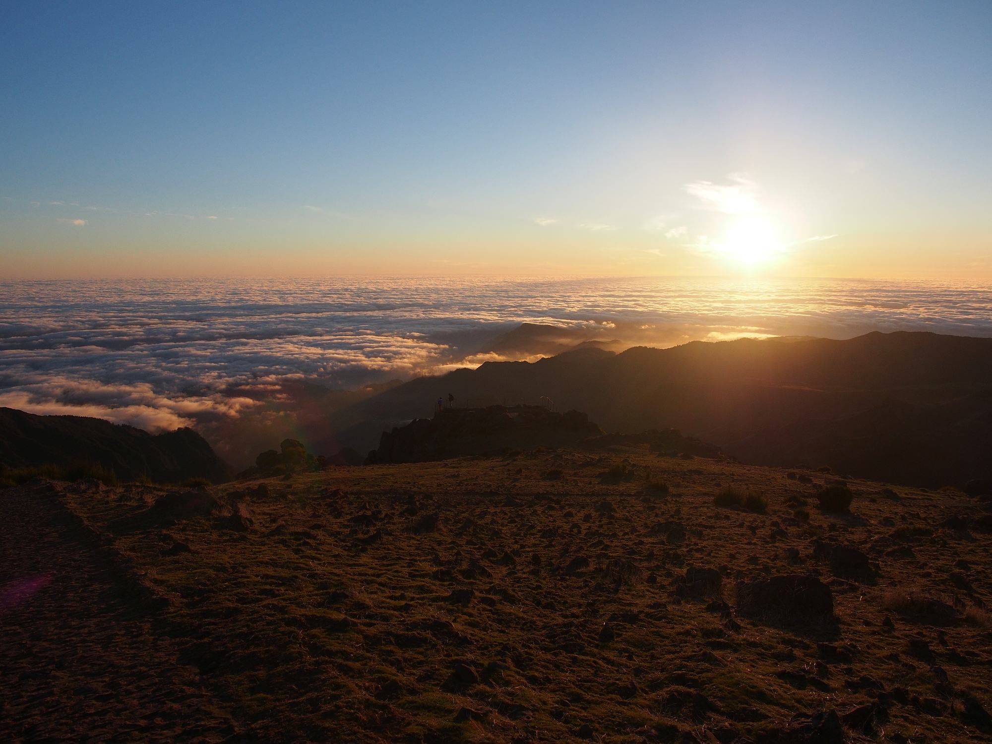 The sun low over a sea of cloud, seen from the grassy slopes by the Pico do Arieiro summit