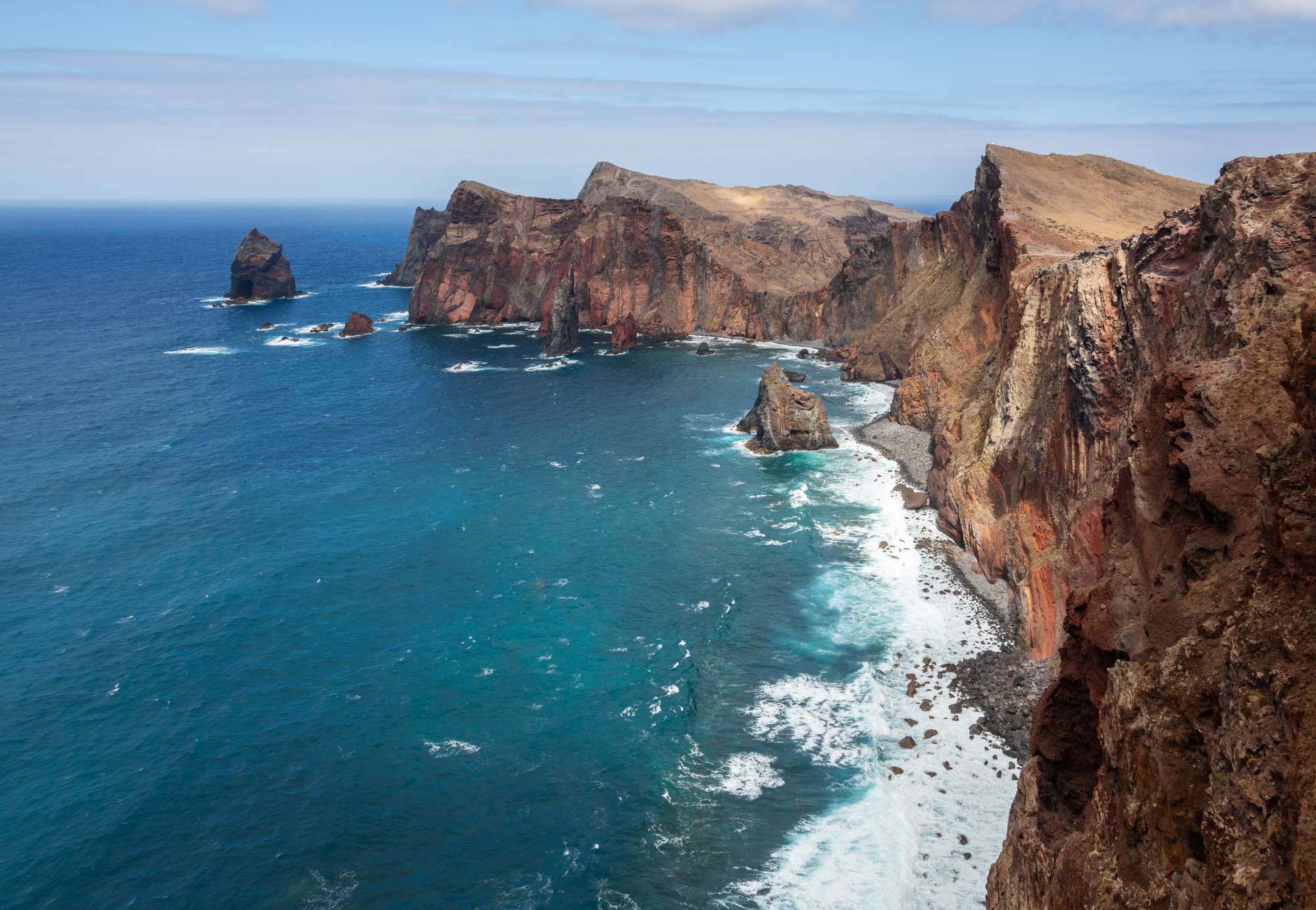 Red and brown cliffs of Ponta de São Lourenço running out to sea stacks in deep blue water