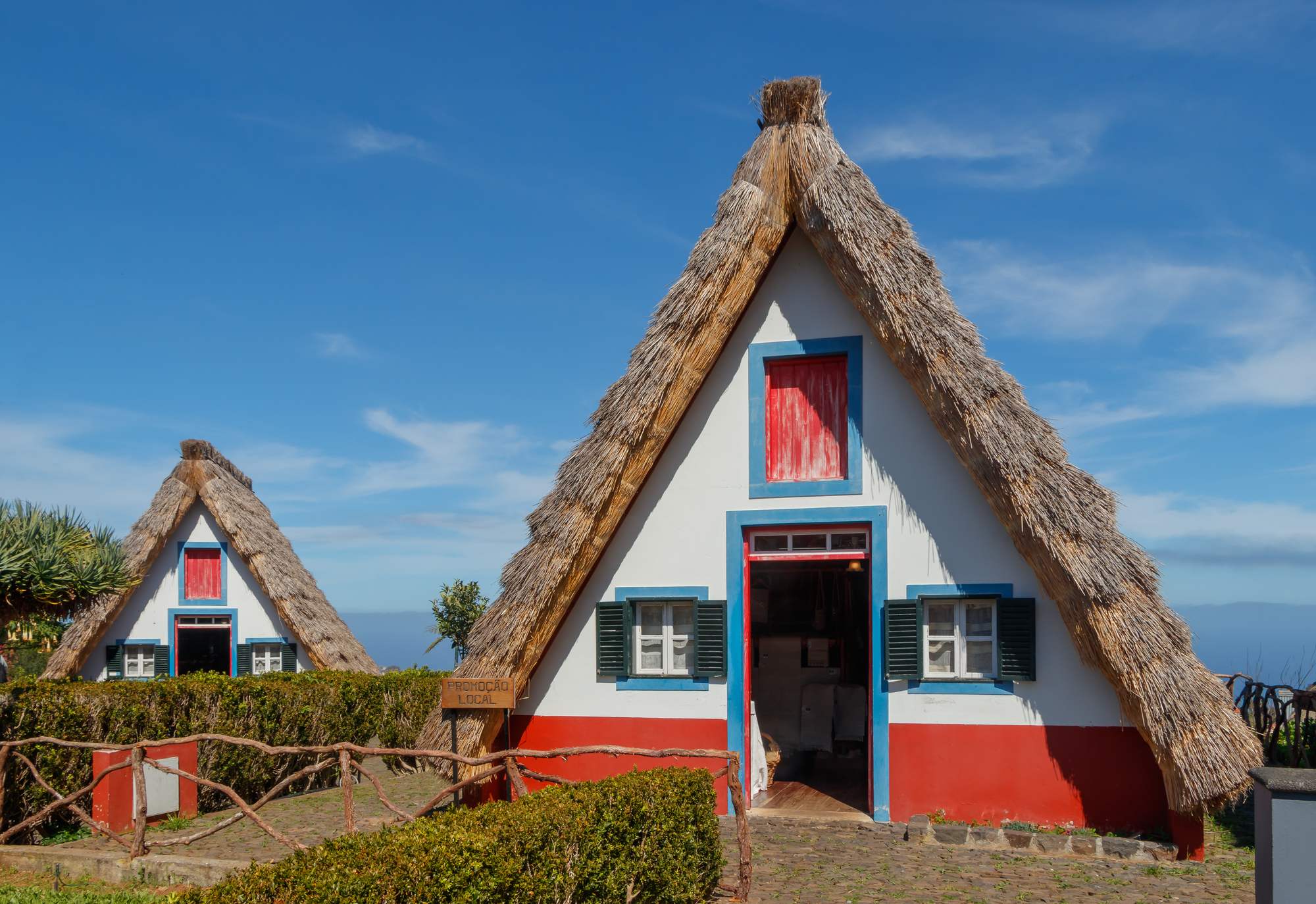 Two thatched A-frame houses in Santana, white with red doors and blue trim, under a clear sky