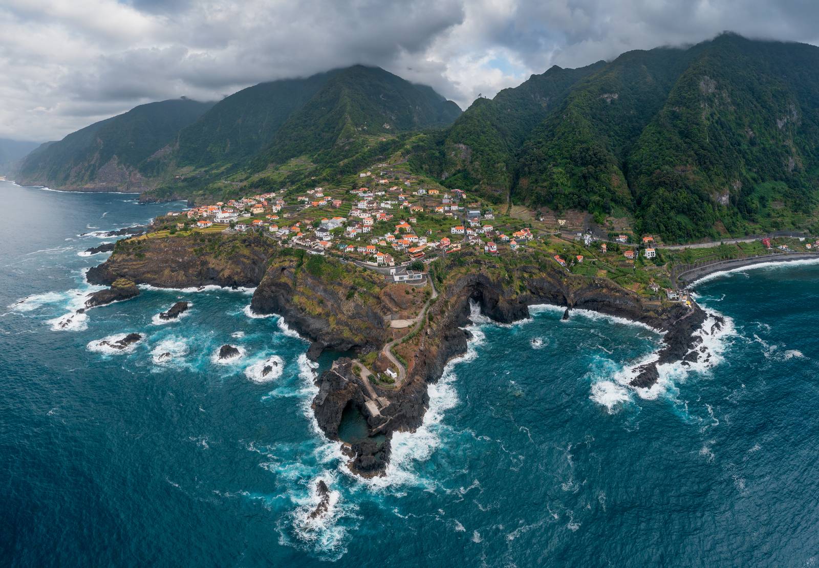 The north coast at Seixal, surf breaking on dark lava rock below steep green cliffs